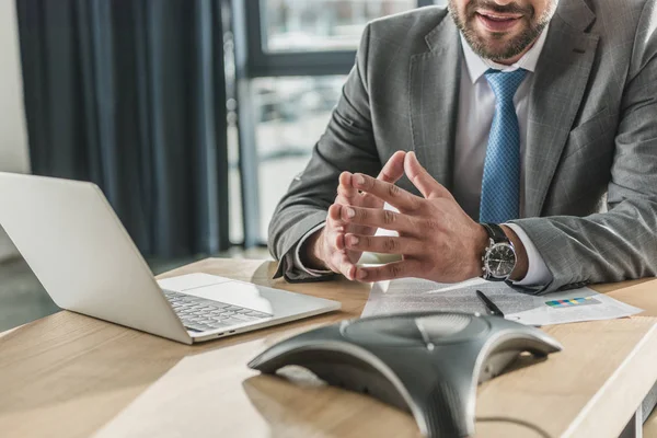 Cropped shot of smiling businessman with laptop and contract using speakerphone at office — Stock Photo