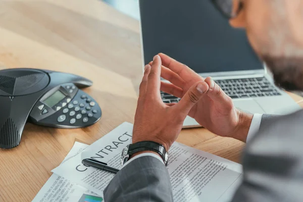 Cropped shot of businessman with laptop and contract using speakerphone at office — Stock Photo