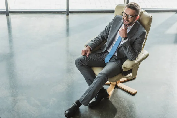 Blick aus der Vogelperspektive auf einen gutaussehenden, glücklichen Geschäftsmann, der im modernen Büro auf einem Luxussessel sitzt — Stockfoto