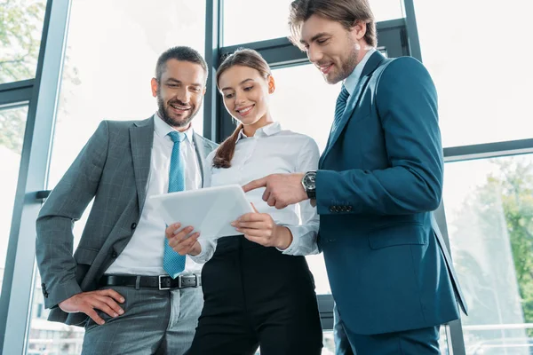 Blick von unten auf zufriedene Geschäftsleute, die gemeinsam Tablet im modernen Büro nutzen — Stockfoto