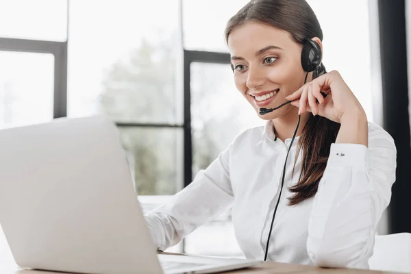 Trabalhador bonito call center feminino com fones de ouvido e laptop sentado no local de trabalho — Fotografia de Stock