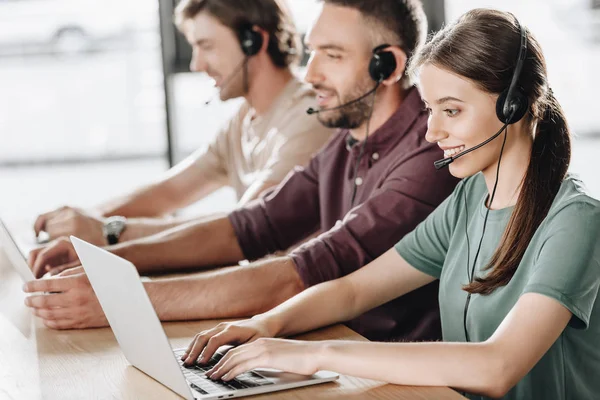 Happy team of call center managers working together while sitting in row at modern office — Stock Photo