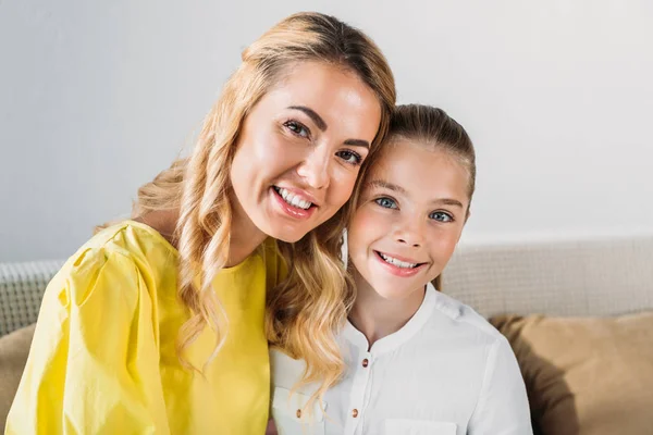 Feliz madre e hija sentadas en el sofá y mirando a la cámara - foto de stock