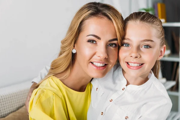 Smiling mother and daughter sitting on couch and looking at camera — Stock Photo