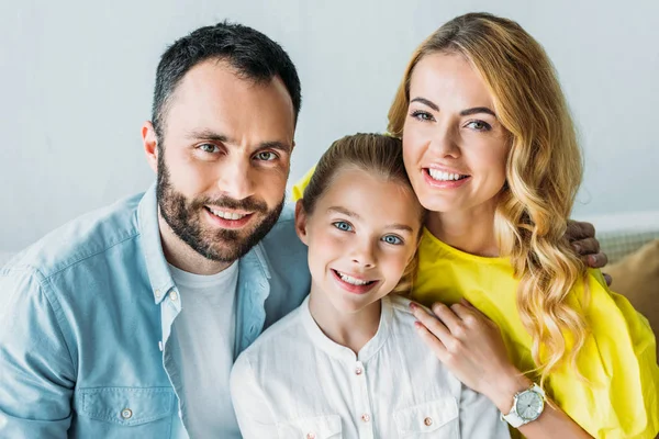 Happy young family sitting on couch together and looking at camera — Stock Photo