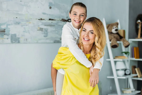 Adorable little daughter embracing mother from behind and looking at camera — Stock Photo