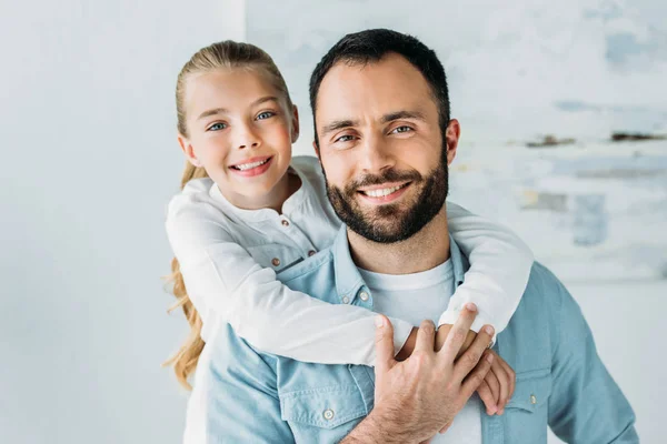 Adorable little daughter embracing father from behind and looking at camera — Stock Photo