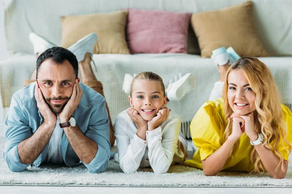 Happy young family lying on floor at home and looking at camera — Stock Photo