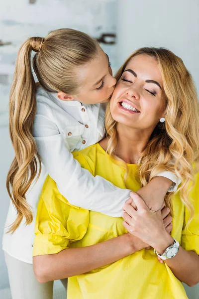 Adorável filhinha abraçando a mãe por trás e beijando-a — Fotografia de Stock