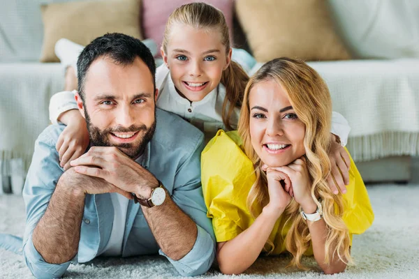 Lächelnde junge Familie liegt zu Hause auf dem Boden und blickt in die Kamera — Stockfoto