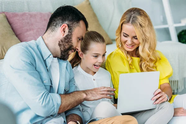Sonriendo familia joven usando el ordenador portátil juntos en casa - foto de stock