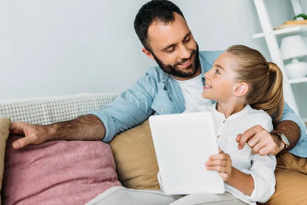 Padre e hija usando la tableta juntos mientras están sentados en el sofá en casa - foto de stock