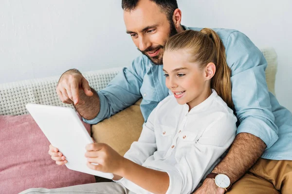 Feliz padre e hija usando la tableta juntos mientras están sentados en el sofá en casa - foto de stock
