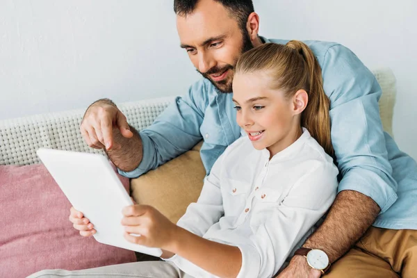 Heureux père et fille en utilisant la tablette ensemble tout en étant assis sur le canapé à la maison — Photo de stock