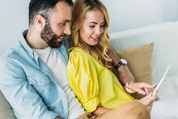 Belo casal usando tablet juntos enquanto sentado no sofá em casa — Fotografia de Stock