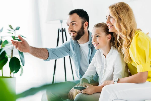 Glückliche junge Familie, die zu Hause gemeinsam fernsieht und auf den Bildschirm zeigt — Stockfoto