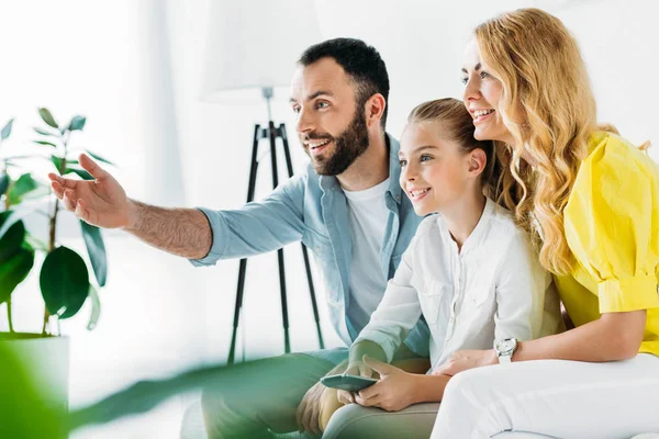 Feliz joven familia viendo la televisión juntos en casa y apuntando a la pantalla - foto de stock