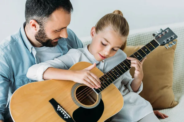 Отец и дочь играют вместе на гитаре дома — стоковое фото