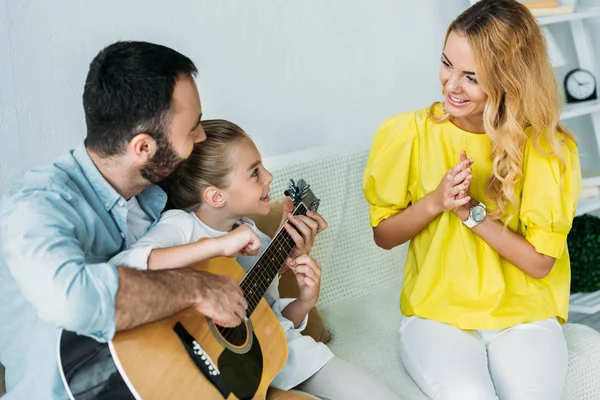 Отец и дочь играют на гитаре для мамы дома, пока она хлопает в ладоши — стоковое фото