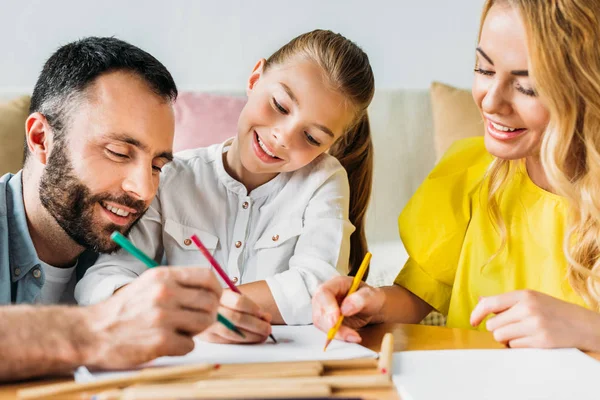 Sonriente joven familia dibujo con lápices de color juntos en casa - foto de stock