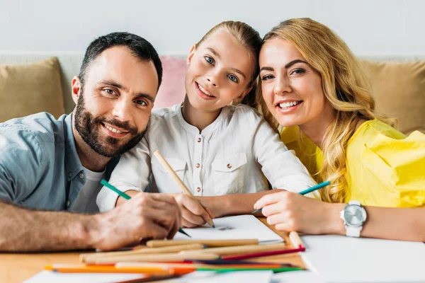 Happy young family drawing with color pencils together and looking at camera — Stock Photo