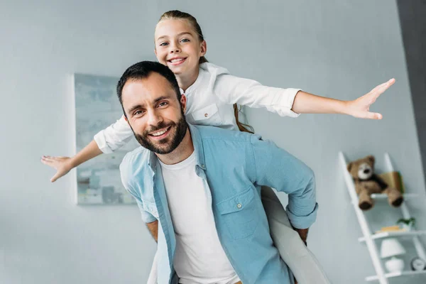 Fille heureuse piggybackking sur père et regarder la caméra à la maison — Photo de stock