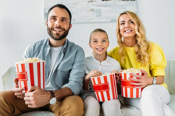 Sonriente joven familia viendo película en casa con cubos de palomitas de maíz - foto de stock