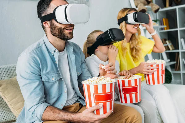 Excited young family in virtual reality headsets watching movie with buckets of popcorn — Stock Photo