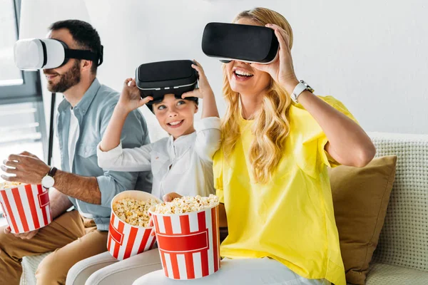 Familia joven feliz en auriculares de realidad virtual con cubos de palomitas de maíz - foto de stock