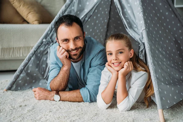 Père et fille couchés sur le sol à l'intérieur du tipi et regardant la caméra à la maison — Photo de stock