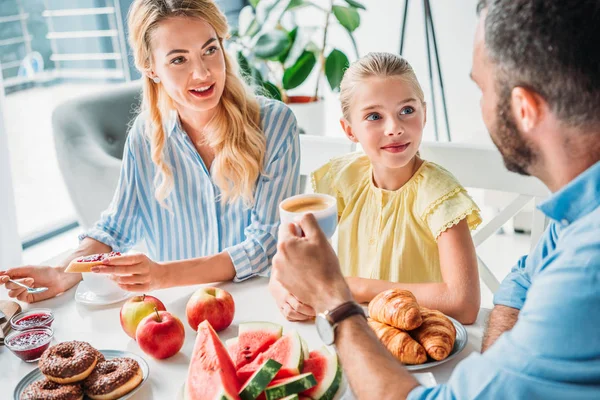 Sonriente familia joven desayunando juntos en casa - foto de stock