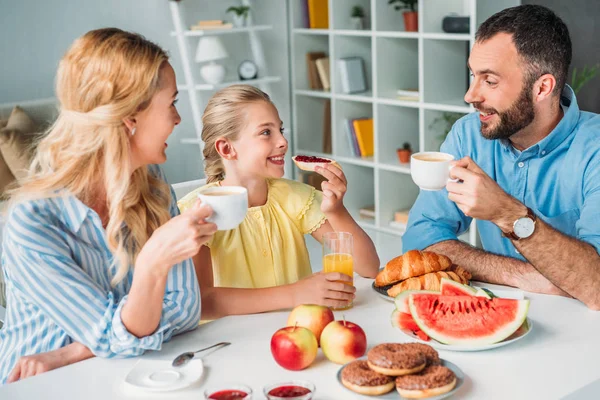 Felice giovane famiglia che fa colazione insieme a casa — Foto stock