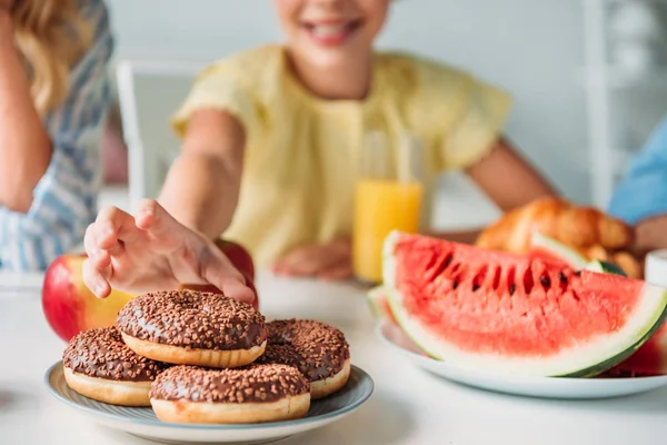 Cropped shot of smiling child reaching for donut during dinner — Stock Photo