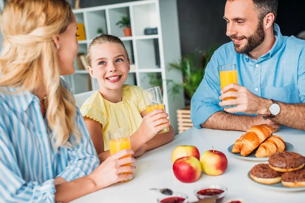 Glückliche junge Familie trinkt frischen Orangensaft zum Frühstück — Stockfoto