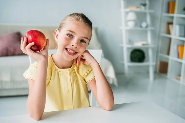 Прелестный маленький ребенок с красным яблоком сидит дома — стоковое фото
