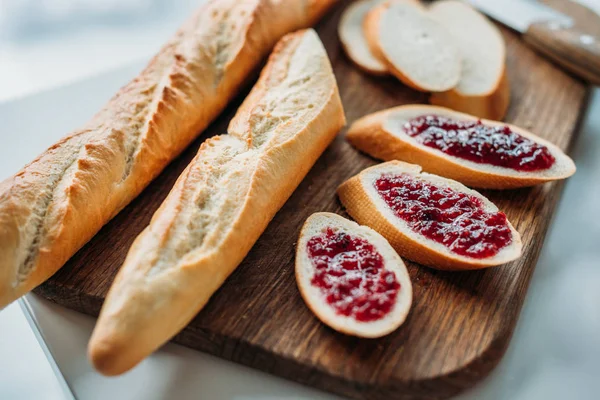 Close-up shot of sliced baguette with jam on wooden cutting board — Stock Photo