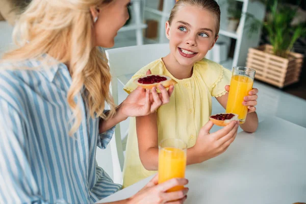 Mãe e filha comendo baguete com geléia e suco de laranja em casa — Fotografia de Stock