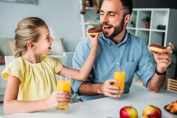 Adorable hija pequeña alimentación padre con donut en casa - foto de stock