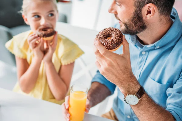 Close-up shot of happy father and daughter eating doughnuts with orange juice at home — Stock Photo