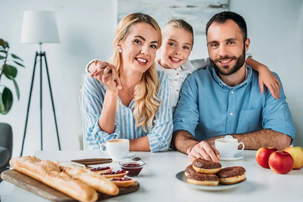 Heureux jeune famille avec petit déjeuner sur la table en regardant la caméra — Photo de stock