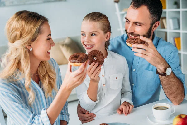 Familia joven feliz comiendo donas glaseadas de chocolate - foto de stock