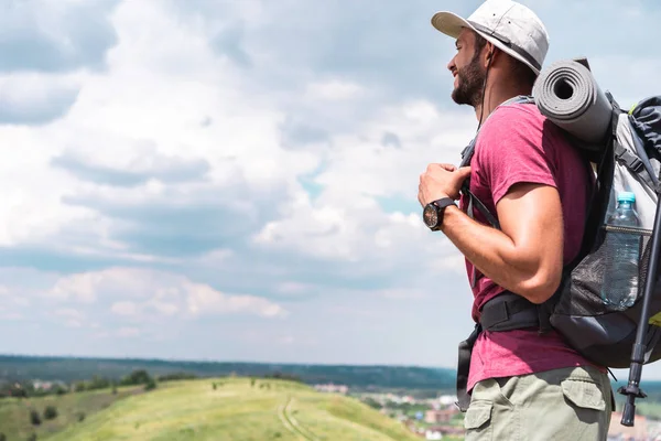 Мужчина турист в шляпе с рюкзаком глядя на летний луг — стоковое фото