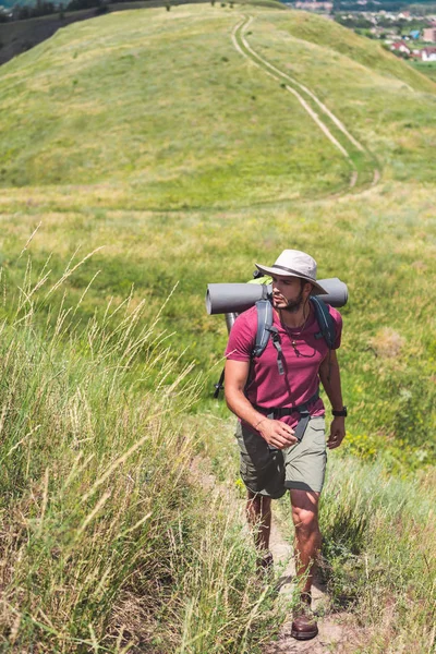 Voyageur en chapeau avec sac à dos et tapis touristique marche sur le chemin — Stock Photo