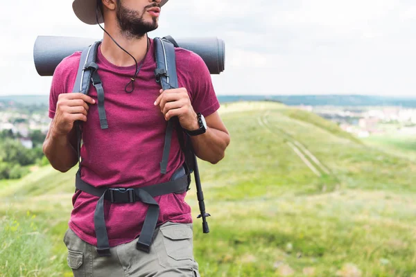 Ausgeschnittene Ansicht eines Reisenden mit Rucksack und Touristenmatte beim Spazierengehen auf der Wiese — Stockfoto