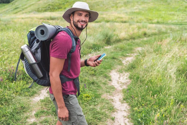 Traveler with backpack using smartphone on summer meadow — Stock Photo