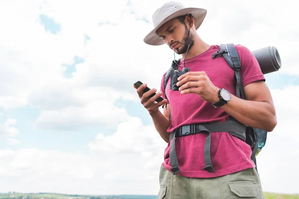 Male traveler with backpack and binoculars using smartphone — Stock Photo