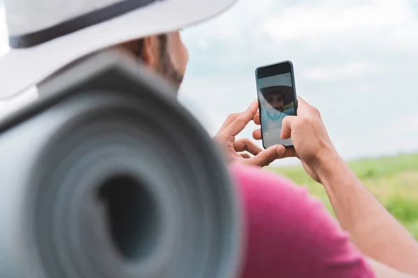 Caminhante com mochila e tapete turístico tomando selfie no smartphone — Fotografia de Stock