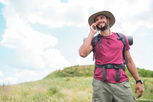 Reisende mit Rucksack telefoniert auf Sommerwiese mit Smartphone — Stockfoto