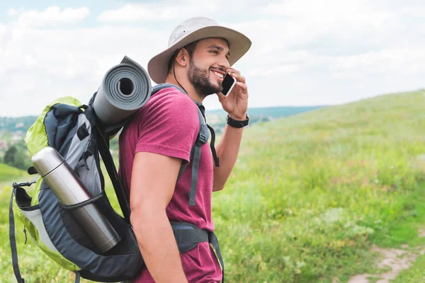 Путешественник с рюкзаком говорит на смартфоне на зеленом лугу — стоковое фото