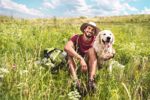Viajero masculino sentado con el perro en el prado verde del verano - foto de stock